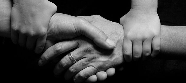 Zwei Kinderhände halten die Hände von zwei Erwachsenen, die sich die Hand reichen