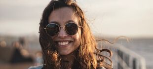Eine Jugendliche mit Sonnenbrille lacht in die Kamera