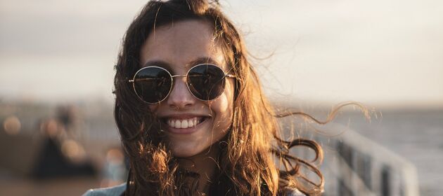 Eine Jugendliche mit Sonnenbrille lacht in die Kamera