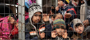 Kinder stehen dicht gedrängt an einem Zaun