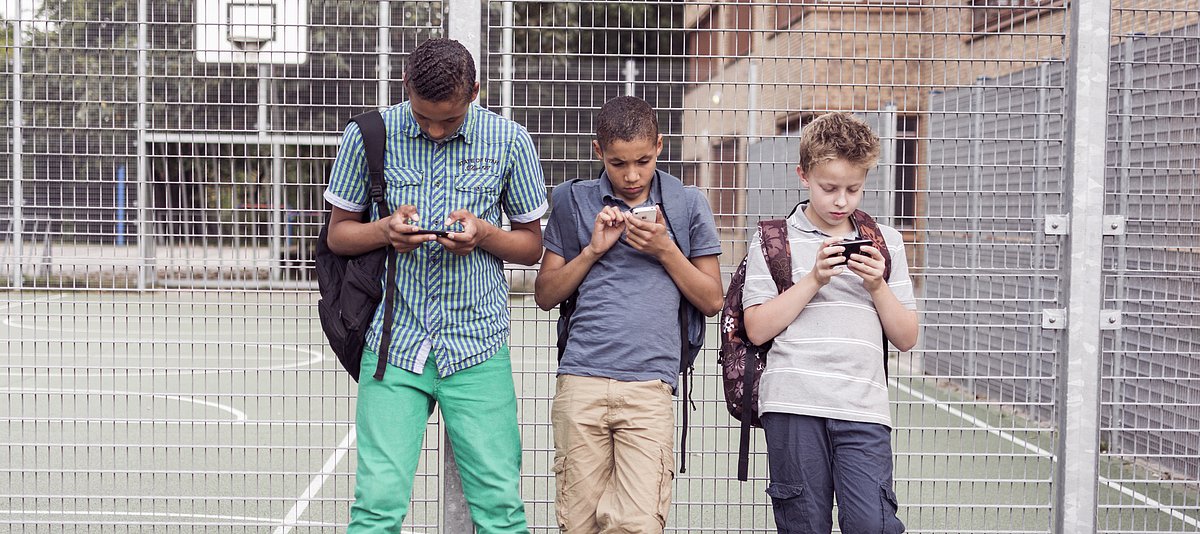 Jugendliche mit Smartphones vor Sportplatz