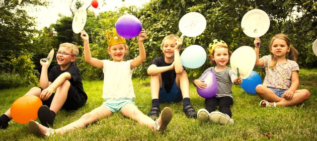 Freudige Kinder mit Luftballons in den Händen sitzen auf deiner Wiese