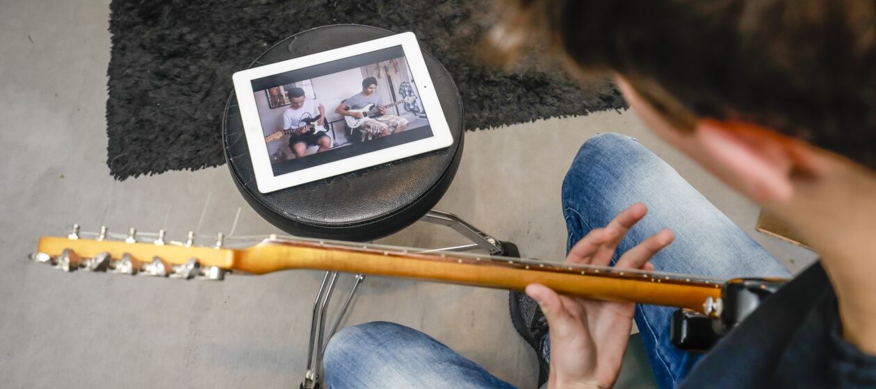 Ein Jugendlicher schaut sich ein Video auf einem Tablet an und bringt sich selbst Gitarrenriffs bei