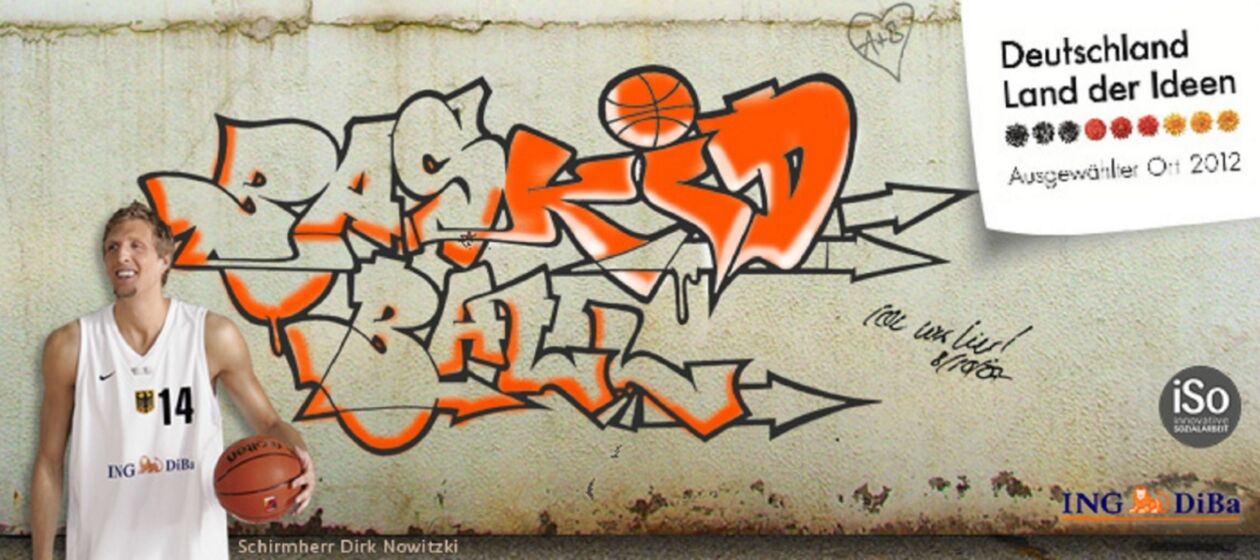 Dirk Nowitzki mit Basketball vor einer Mauer mit Graffitti