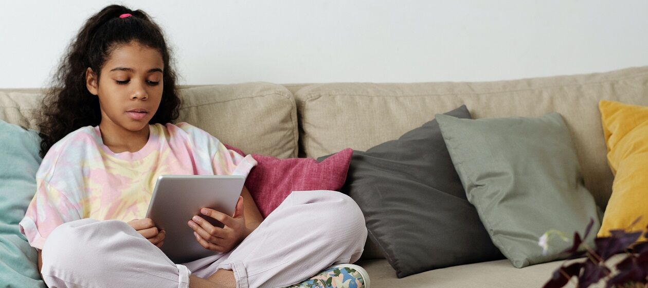 Mädchen sitzt mit Tablet in der Hand auf einem Sofa
