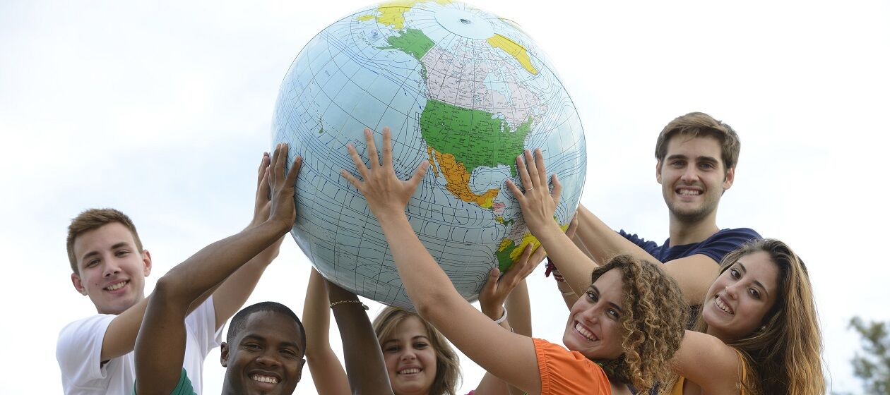 Sechs junge Erwachsene verschiedener Herkunft halten einen großen Globus-Ball hoch.
