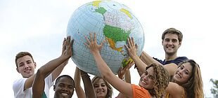 Sechs junge Erwachsene verschiedener Herkunft halten einen großen Globus-Ball hoch.