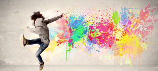 Eine Jugendlicher im Kapuzenpullover springt vor einer Wand mit einem Graffiti hoch.