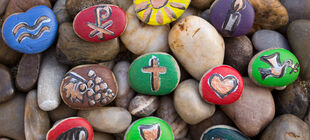 Steine, die mit christlichen Symbolen bemalt sind, liegen auf einem Steinbett. 