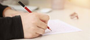 Ein Blatt Papier liegt auf einem Schreibtisch und wird mit einem Bleistift beschriftet.