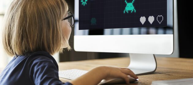 Mädchen mit Brille sitzt vor einem Computerbildschirm und spielt ein Computerspiel