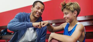 Ein Trainer und ein Junge mit einem Basketball auf den Beinen halten nach dem Training lächelnd ihre Fäuste gegeneinander