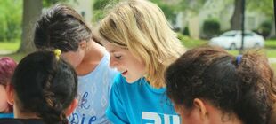 Eine junge, blonde Frau mit einem Freiwilligen-T-Shirt steht inmitten einer Gruppe Mädchen.