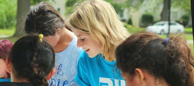 Eine junge, blonde Frau mit einem Freiwilligen-T-Shirt steht inmitten einer Gruppe Mädchen.