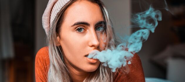 Eine junge Frau schaut in die Kamera während sie Rauch aus ihrem Mund bläst