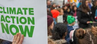 Auf einer Demo wird ein Schild hochgehalten auf dem steht in englsicher Sprache climate action now