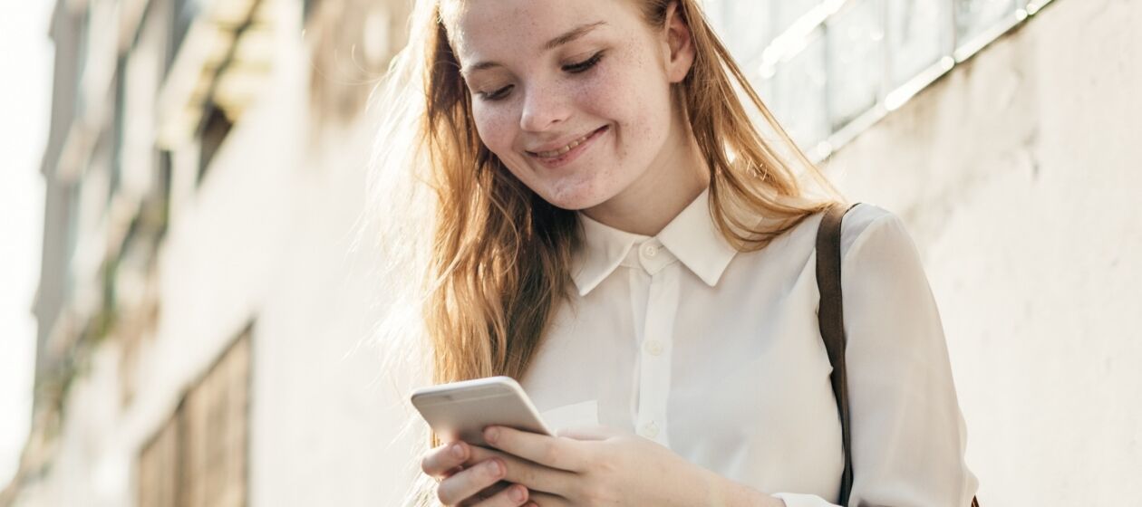 Jugendliche in Stadtumgebung sieht lächelnd auf ihr Smartphone