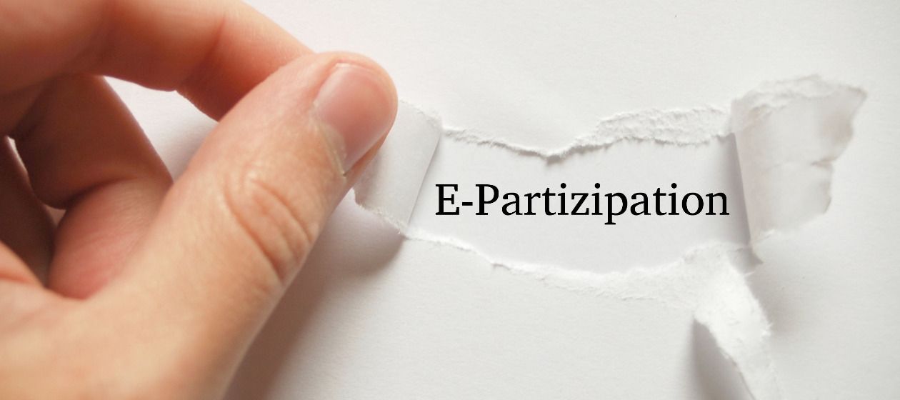Eine Hand reißt ein Stück Papier ab, darunter erscheint das Wort 'E-Partizipation'
